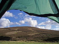 Sunny view from tent of hill with blue sky and white clouds