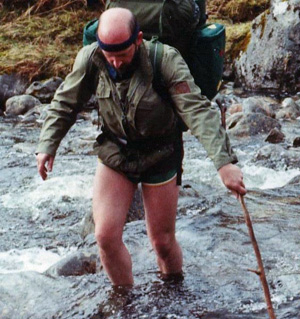 Mic Connel in shorts fording a swollen river