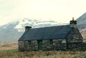 Meananach Bothy A remote building with snow covered mountains in background.